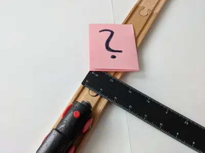 A wooden toy train. A measuring ruler is placed on the tracks, with a post-it note with a question mark.