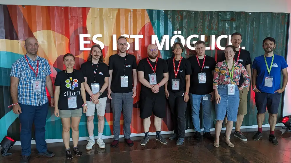 The 10 members of the team pose in front of a decorated container wall reading “Es ist möglich”.